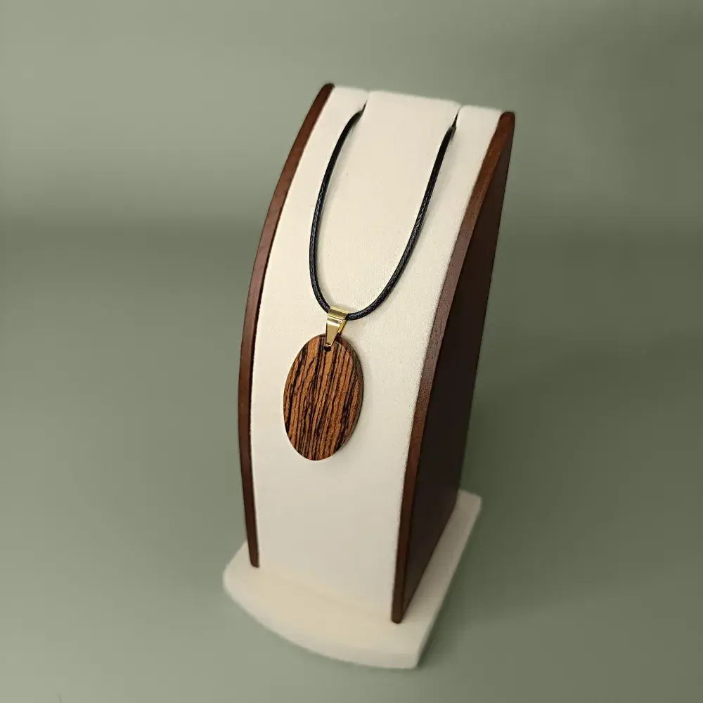 Vue latérale et plongeante du pendentif Écorce d’Or en bois de Bocote, forme ovale, veinages noirs et dorés subtils.