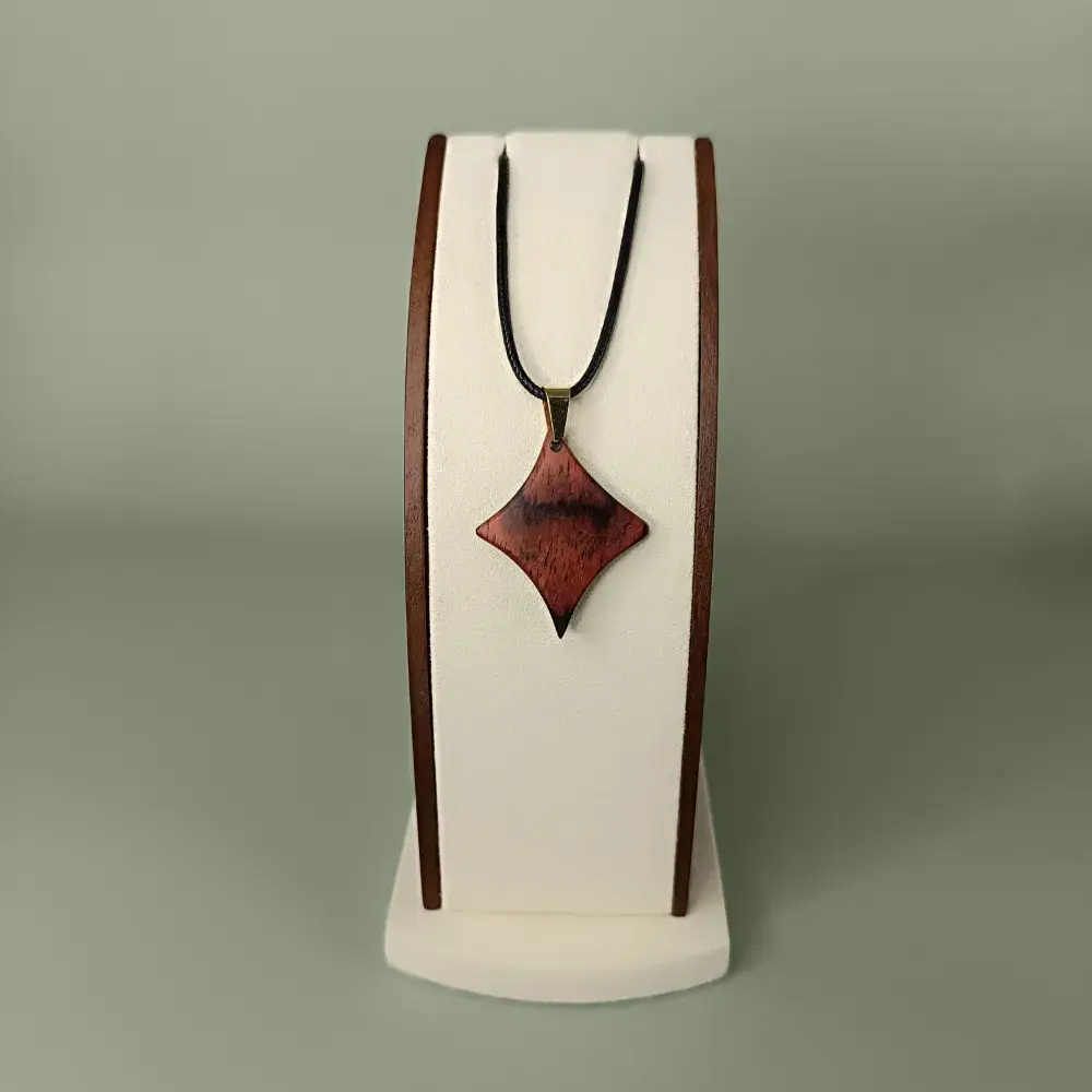 Vue de face du pendentif Braise Étoilée en bois de Cocobolo, forme étoile à quatre branches, veinages rouges et orangés.