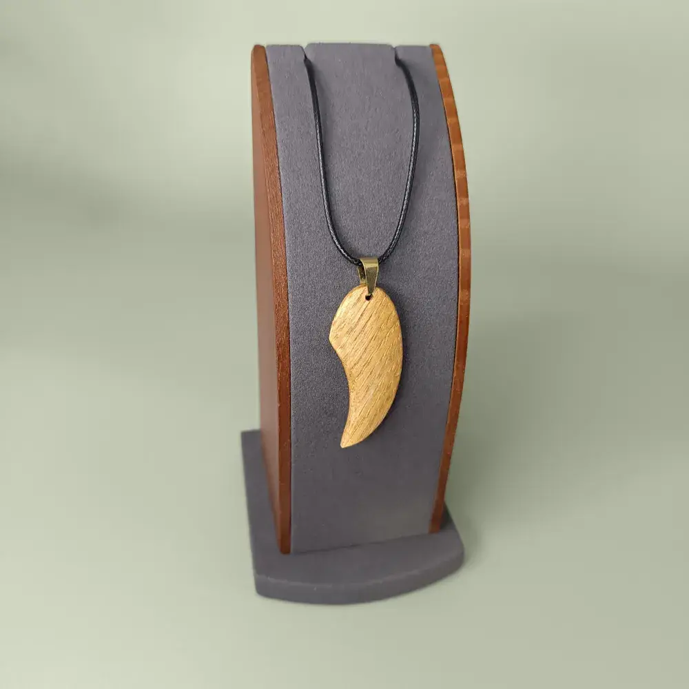 Bijou artisanal pendentif Élan Courbé en bois naturel sur son présentoir.