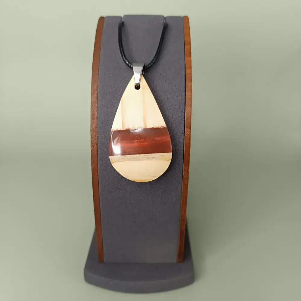 Pendentif en bois de pin et résine époxy rouge-orangé sur présentoir, vue de face.