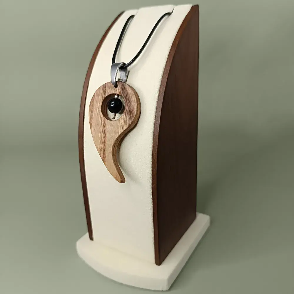 Pendentif en bois naturel avec obsidienne noire, présenté légèrement de côté et en plongée sur un présentoir, semi-luxueux et élégant.