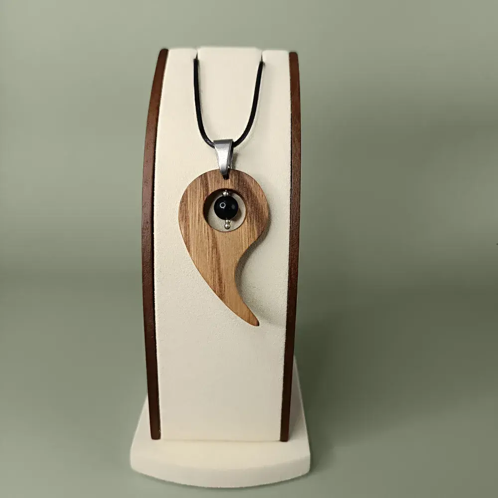 Pendentif en bois naturel avec obsidienne noire, présenté de face sur un présentoir, semi-luxueux et élégant.