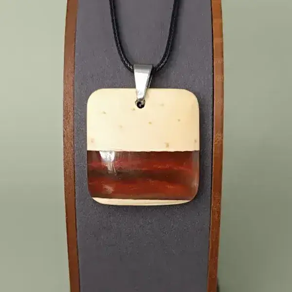 Pendentif carré en bois de pin et résine rouge-orange sur présentoir, bijou artisanal et poétique.