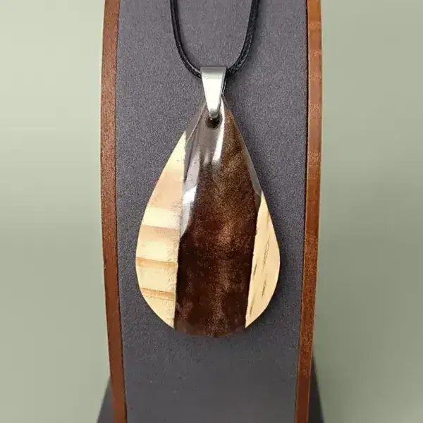 Pendentif en bois de pin et résine marron sur présentoir, bijou artisanal et poétique.