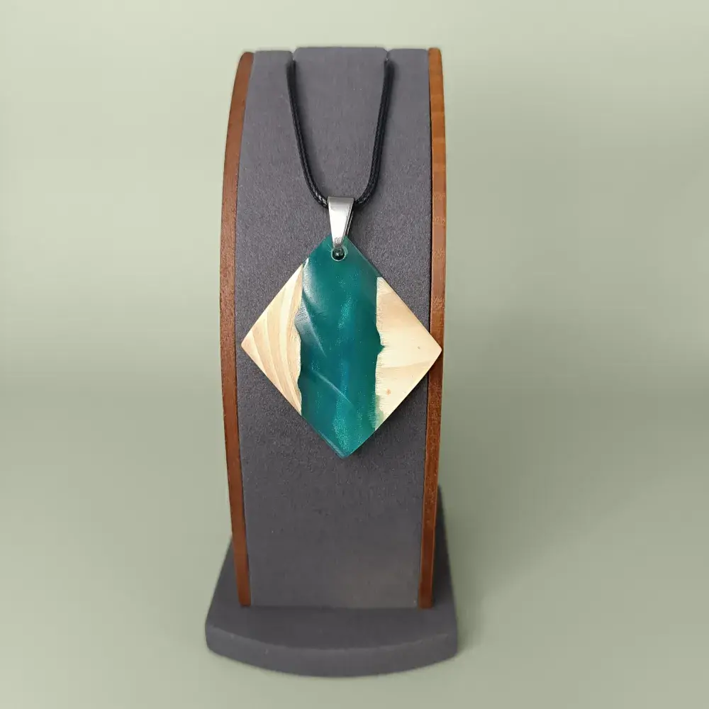 Pendentif artisanal en bois et résine turquoise vue de face sur présentoir.