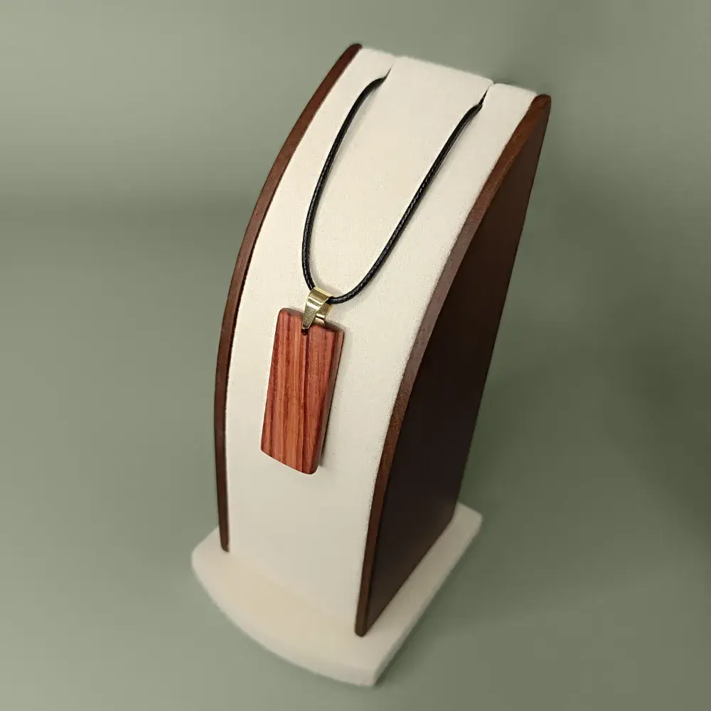 Vue latérale et plongeante du pendentif Éclat Rosé en bois de rose, forme rectangulaire aux coins arrondis, veinages brun rosé et rouge doux.