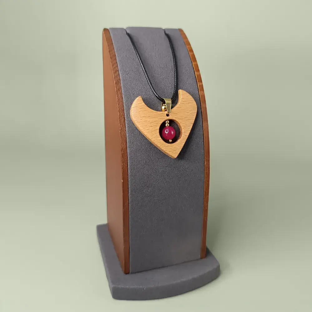 Pendentif en bois naturel avec rubis chauffé, forme de cœur, présenté légèrement de côté sur un présentoir, semi-luxueux et poétique.