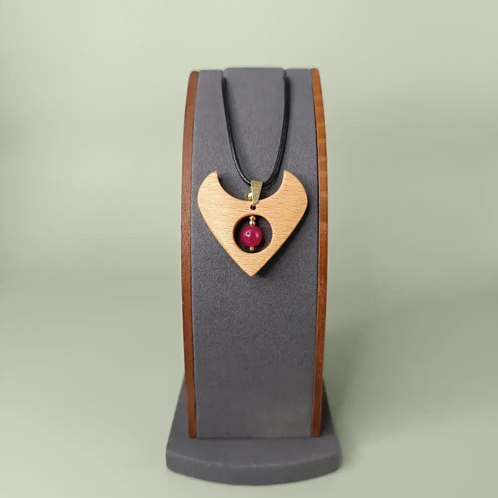 Pendentif en bois naturel avec rubis chauffé, forme de cœur, présenté de face sur un présentoir, semi-luxueux et poétique.
