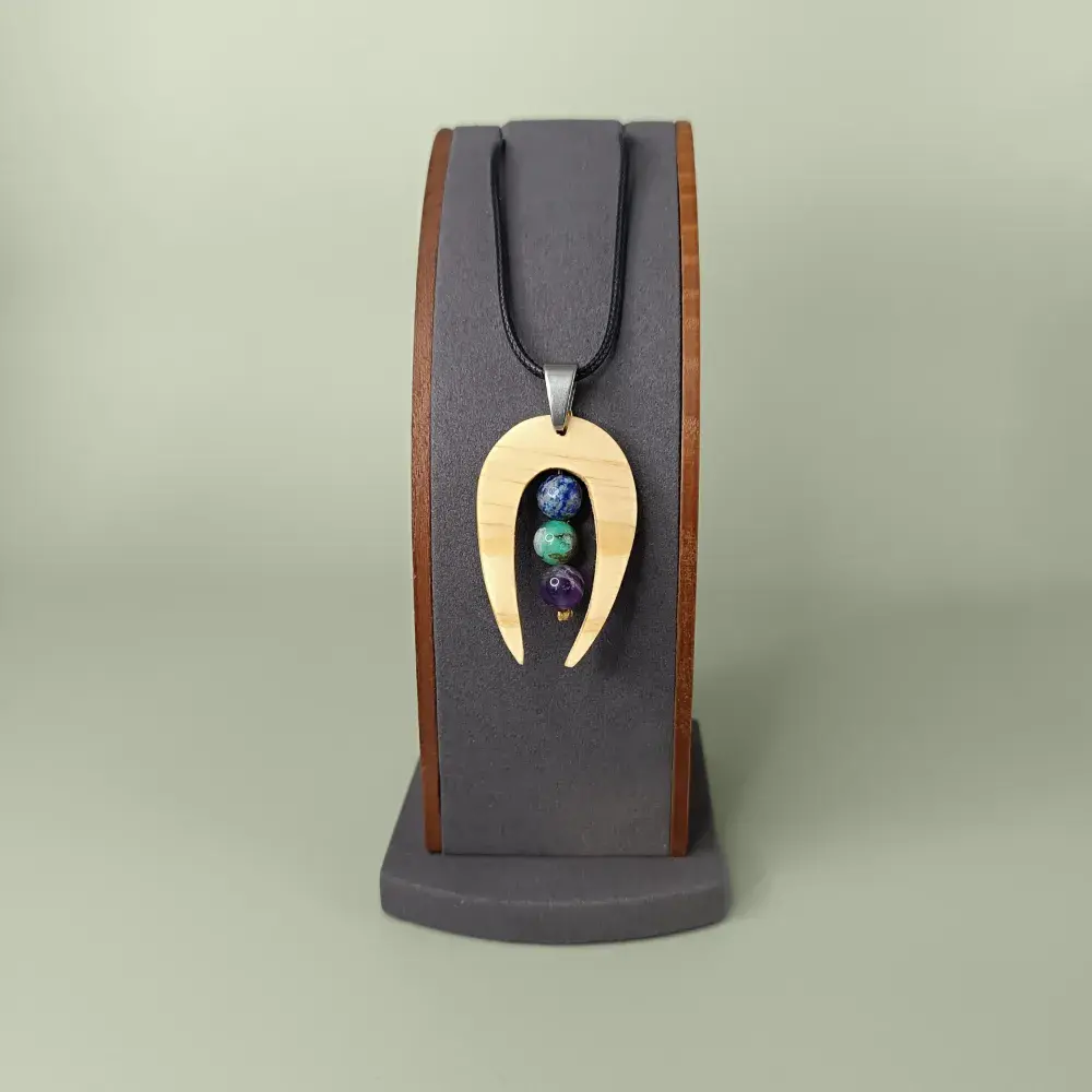 Pendentif en bois naturel avec trois pierres fines, présenté de face sur un présentoir, artisanal et élégant.