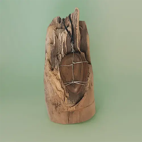 Vue arrière du pendentif Étreinte d’Acier en noyer, avec son montage en fil d’acier inoxydable 316L, sur un support en bois flotté.