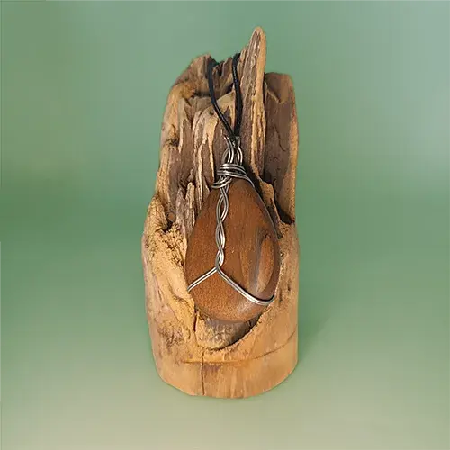 Vue arrière du pendentif Noyer Enlacé en noyer, avec son montage en fil d’acier inoxydable 316L, sur un support en bois flotté.